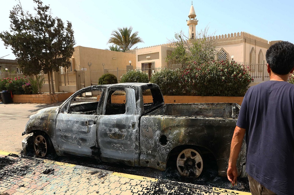 Seorang pria berjalan di dekat sebuah mobil yang terbakar dalam bentrokan antar faksi bersenjata di Tripoli, Libya -- MAHMUD TURKIA / AFP
