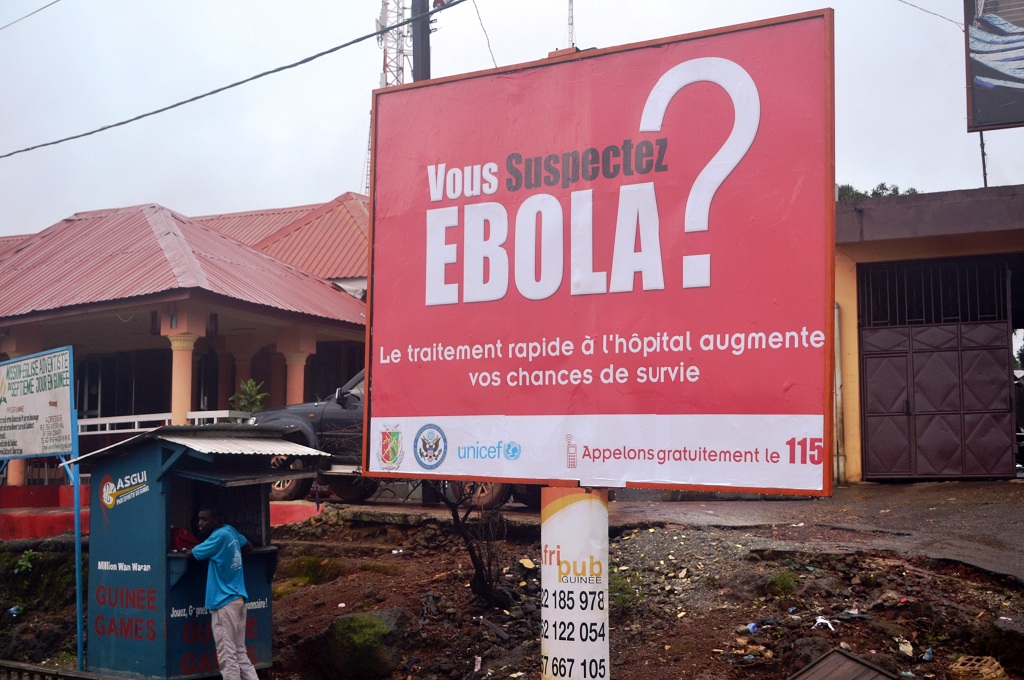 Seorang pria berdiri di samping billboard besar mengenai virus Ebola di Conakry, Guinea -- CELLOU BINANI / AFP