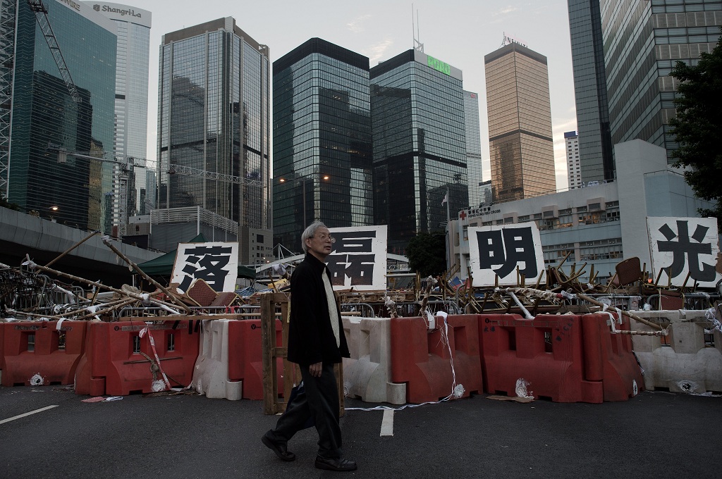 Seorang warga melintas di depan barikade yang dipasang demonstran pro demokrasi di distrik Admiralty, Hong Kong - AFP/NICOLAS ASFOURI