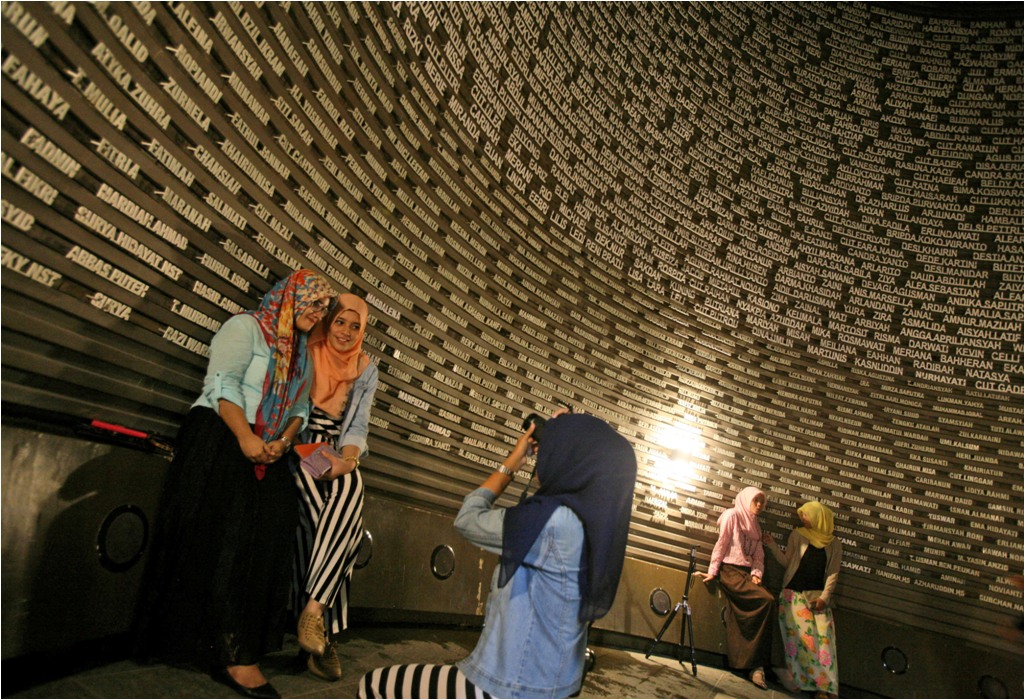 Warga berfoto membelakangi nama-nama korban meninggal dan hilang akibat tsunami Aceh, 26 Desember 2014, di Museum Tsunami Aceh, Banda Aceh, Rabu (24/12/2014). AP/Binsar Bakkara