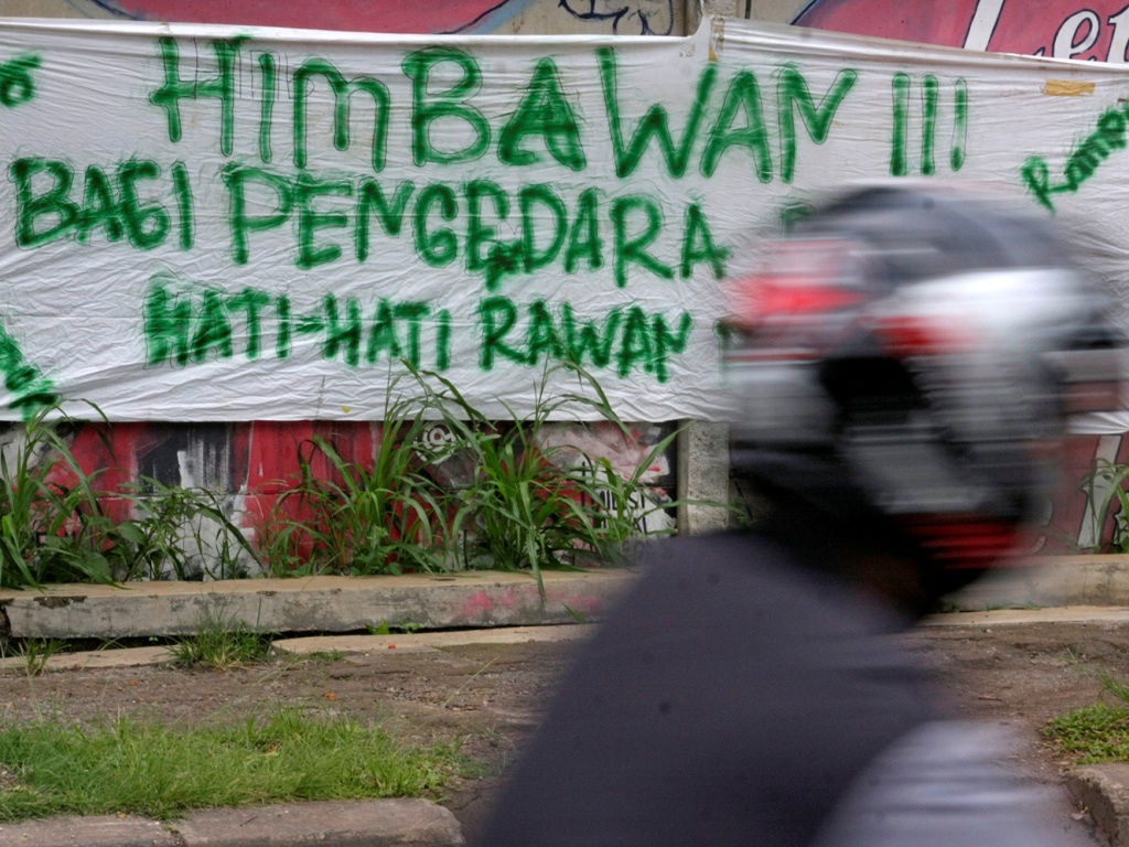 Pengendara motor melintas di dekat spanduk himbauan bagi pen gendara roda dua hati-hati rawan begal dan rampok di Jalan Juan da, Depok. (Foto:MI/Barry)