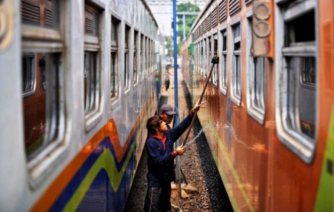 Petugas kebersihan tengah membersihkan gerbong-gerbong kereta api. 