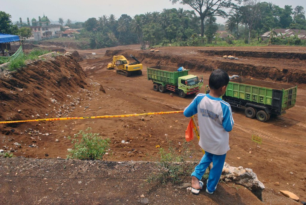 Siswa SD menyaksikan sejumlah truk dan alat berat mengangkut pasir dalam proyek pembangunan Jalan Tol Bogor-Ciawi-Sukabumi (Bocimi) di Kampung Harjasari, RT 01 RW 06, Kota Bogor, Jawa Barat, Selasa (3/11). Foto: Antara/Arif Firmansyah