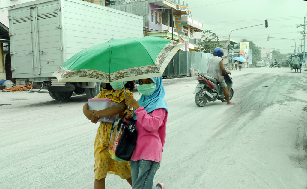 Warga menggunakan masker dan payung saat abu vulkanik Gunung Dukono melanda Kecamatan Tobelo Utara pada Jumat (25/5/2012). (Media Indonesia/Panca Syurkani)