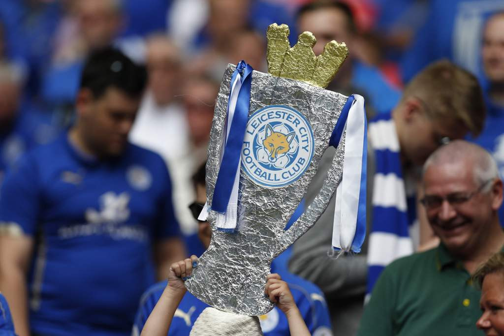 Salah seorang fan Leicester City mengangkat replika trofi kampiun Liga Primer Inggris yang mereka raih musim lalu (Foto: AFP PHOTO / Ian Kington)