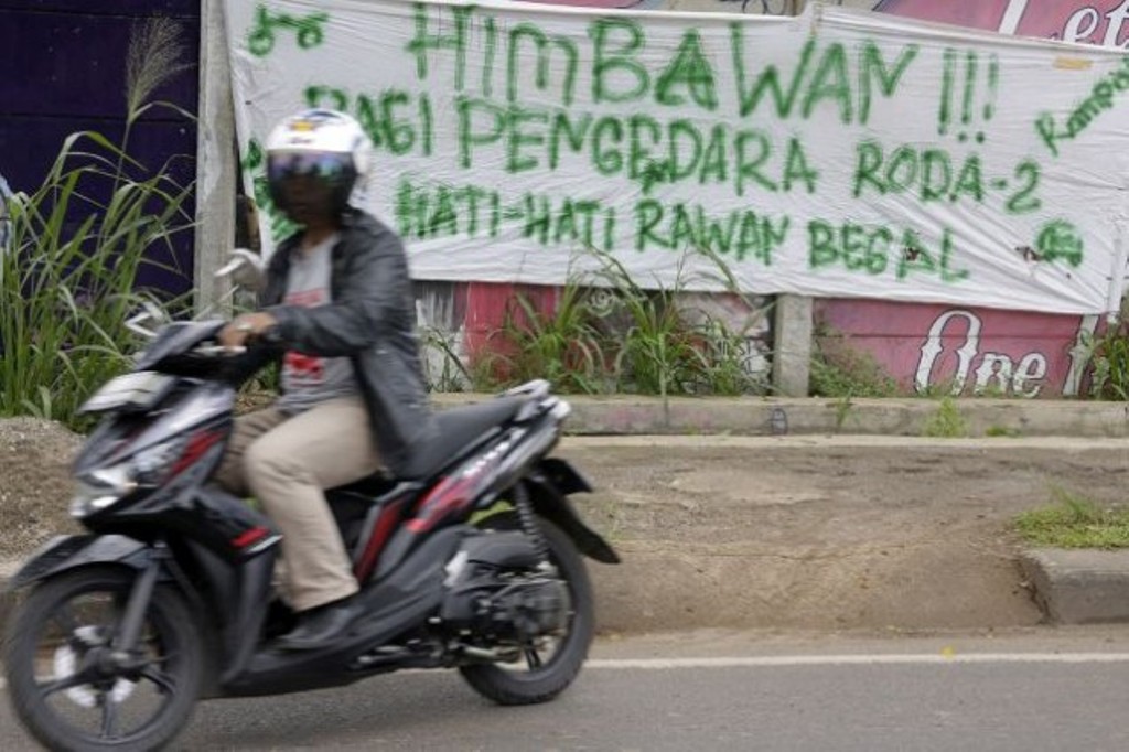 Pemotor melintas di dekat spanduk imbauan berhati-hati di daerah rawan begal di Jalan Juanda, Depok, Jawa Barat. (Foto: MI/Bary Fathahilah)