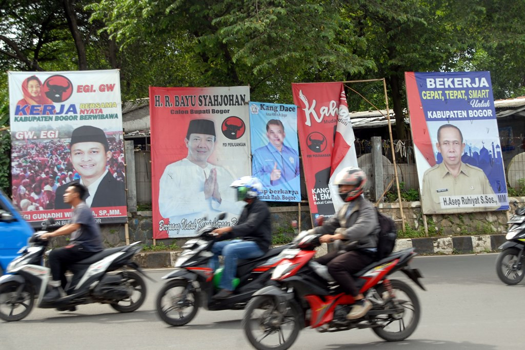 Pengendara sepeda motor melintas di depan baliho bakal calon peserta Pilkada serentak 2018 di Jalan KSR Dadi Kusmayadim Cibinong, Kabupaten Bogor, Jawa Barat. (Foto: ANTARA/Yulius Satria)