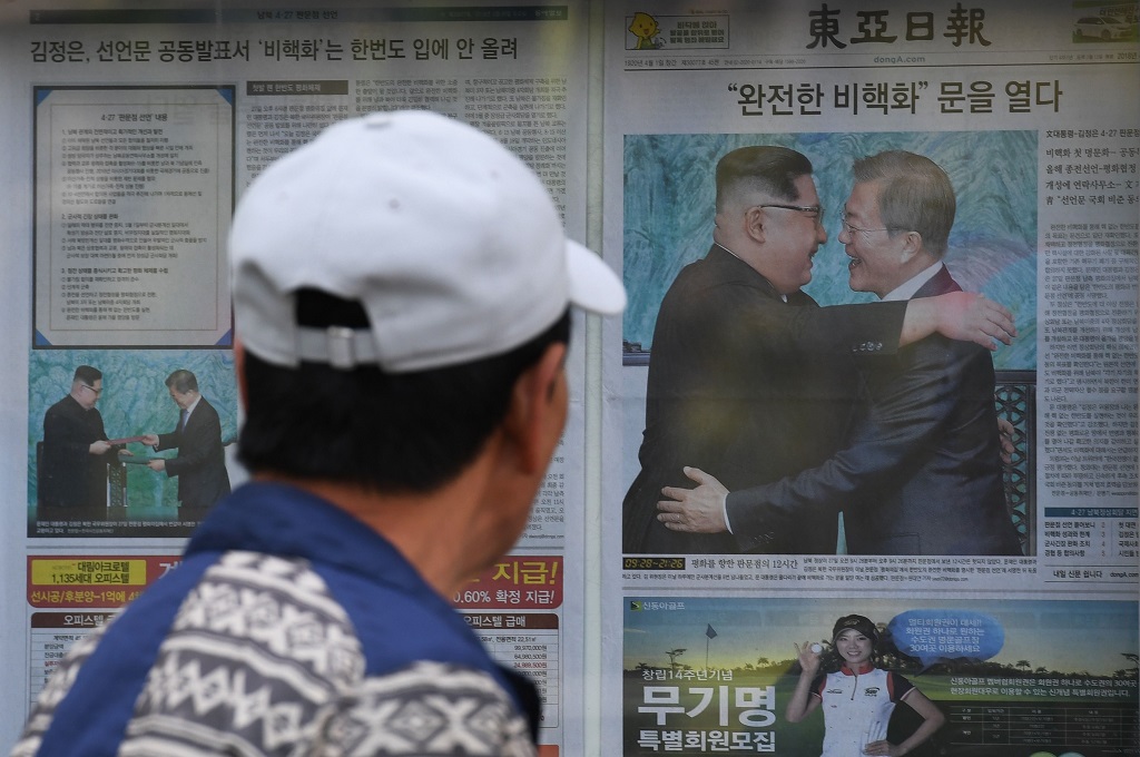 Seorang warga di Seoul, Korsel, 28 April 2018, berjalan melewati surat kabar yang melaporkan pertemuan Kim Jong-un dengan Moon Jae-in. (Foto: AFP/GREG BAKER)