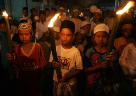 Tiga anak membawa obor yang diiringi oleh ratusan warga lainnya