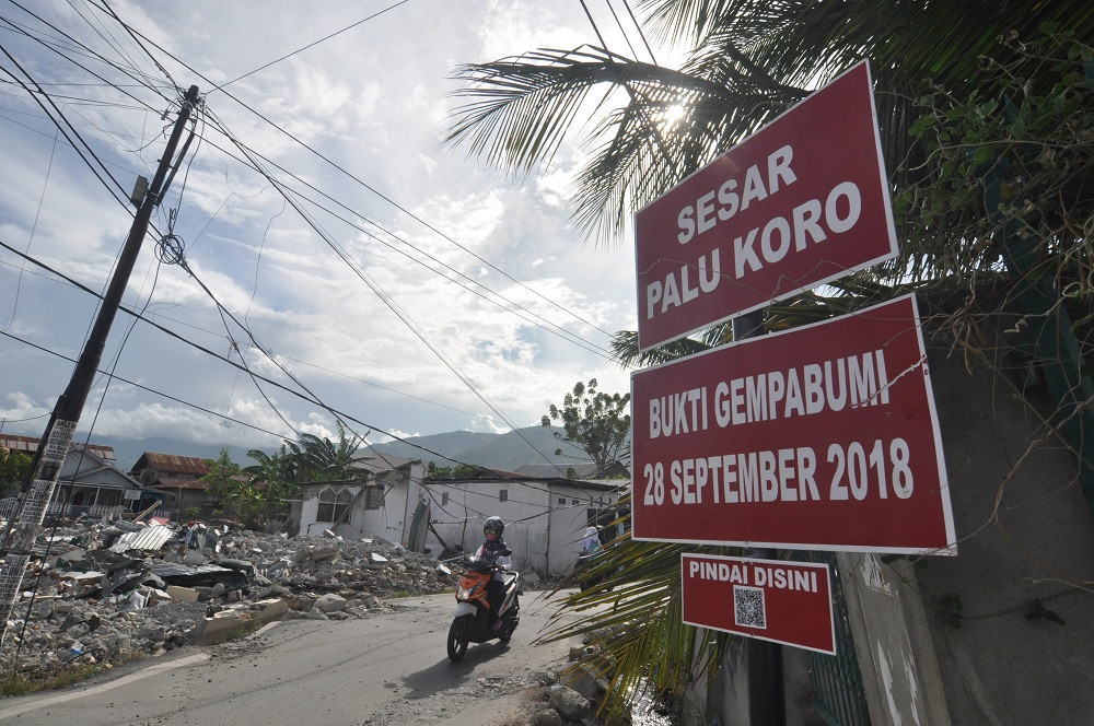 Pengendara melintas di dekat papan informasi digital tentang keberadaan dan jalur sesar palu Koro segmen palu yang dipasang di salah satu lokasi yang rusak akibat gempa di Palu, Sulawesi Tengah, Selasa (11/12/2018). ANTARA FOTO/Mohamad Hamzah.