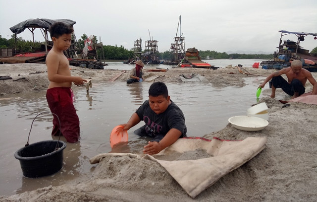 Dua bocah pelajar SD, Budi (kiri), 9, dan Ramadhan (tengah), 9, mengumpulkan sisa pasir pembuangan limbah dari mesin tambang untuk mencari butiran timah di pesisir Sungai Pangkalarang, Kecamatan Pangkalbalam, Pangkalpinang, Babel.