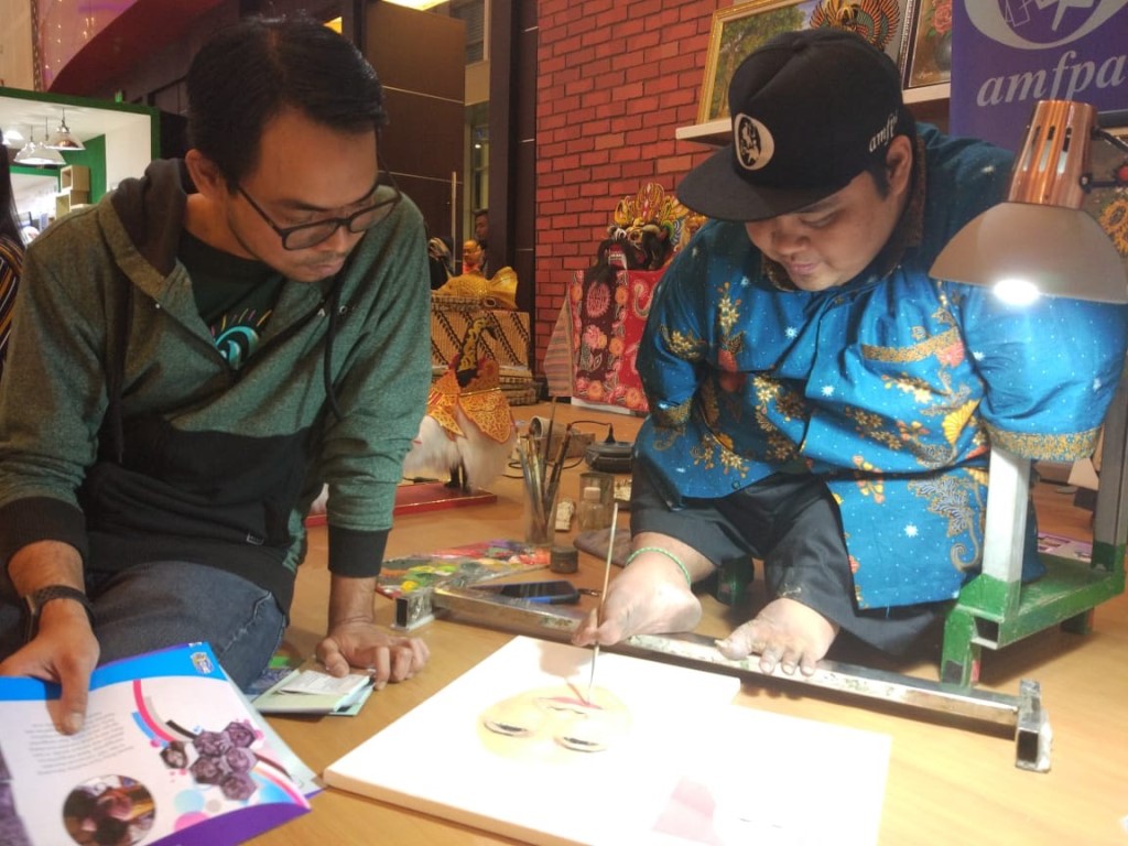 Seorang pengunjung memperhatikan pelukis difabel di Jatim Fair, Surabaya. (Foto: Medcom.id/Amaluddin)