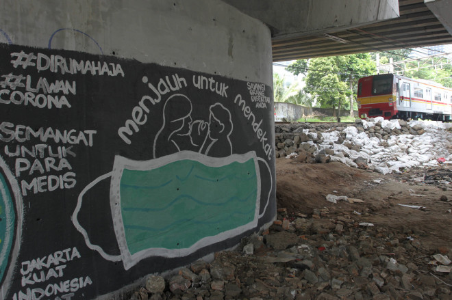 Warga melintasi mural ajakan untuk menggunakan masker dan tetap di rumah di kolong Jalan Rasuna Said, Jakarta.