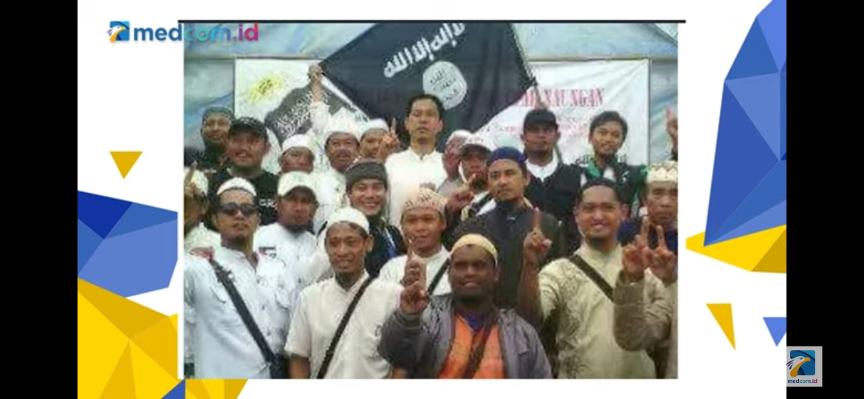 Munarman berfoto di depan bendera ISIS sambil mengacungkan jari telunjuk. Medcom.id/Candra Yuri Nuralam