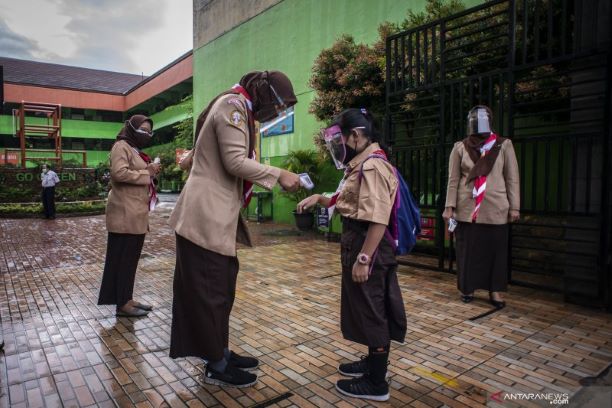 Guru sedang mengecek suhu tubuh siswa saat uji coba PTM Terbatas di Jakarta. Foto: ANT/Aprilio Akbar