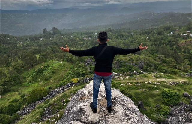 Pengunjung menikmati pesona alam dari ketinggian dengan berdiri di atas batu bekas tambang marmer Desa Tunua. (Foto: Dok. Arthurio Oktavianus)