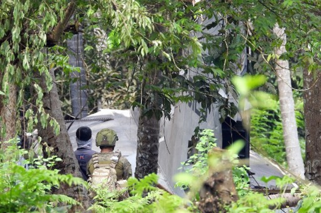 Prajurit Filipina berdiri di dekat puing pesawat kargo yang jatuh di pulau Jolo pada Minggu, 4 Juli 2021. (Nickee BUTLANGAN / AFP)