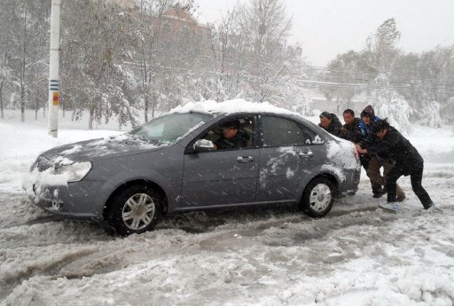 Warga mendorong sebuah mobil yang mogok akibat badai salju. Foto: AFP