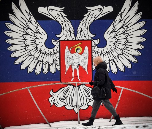 Warga Ukraina berjalan dengan latar belakang bendera Ukraina di Donetsk. Foto: AFP