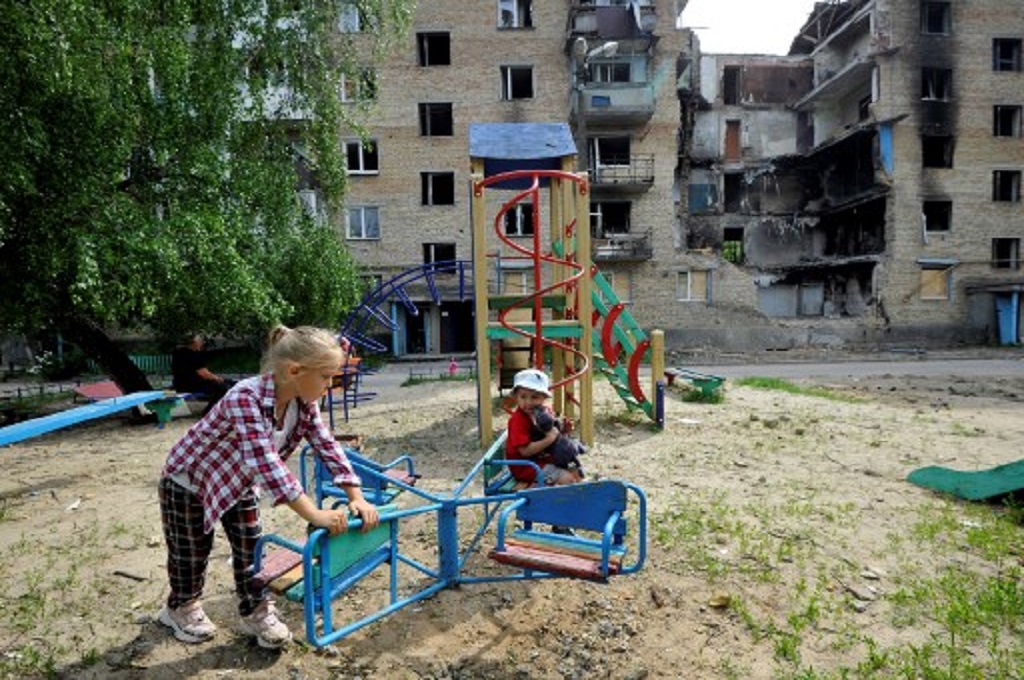 Anak-anak bermain di depan sebuah bangunan yang rusak di desa Horenka, Ukraina, 4 Juni 2022. (Sergei CHUZAVKOV / AFP)