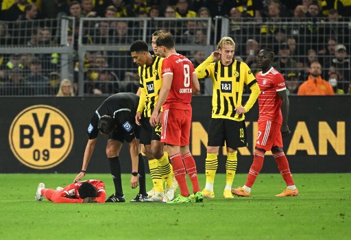 Bek Bayern Muenchen Alphonso Davies terkapar setelah dilanggar pemain Borussia Dortmund Jude Bellingham. (INA FASSBENDER / AFP)