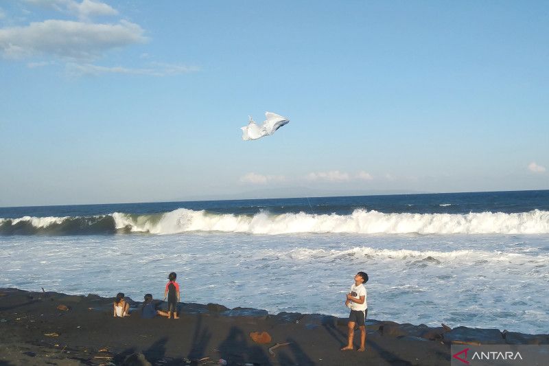 Warga bermain layang-layang dengan latar belakang ombak tinggi di Pantai Purnama, Kabupaten Gianyar, Bali, Minggu, 14 Mei 2023. Antara/Dewa Ketut Sudiarta Wiguna