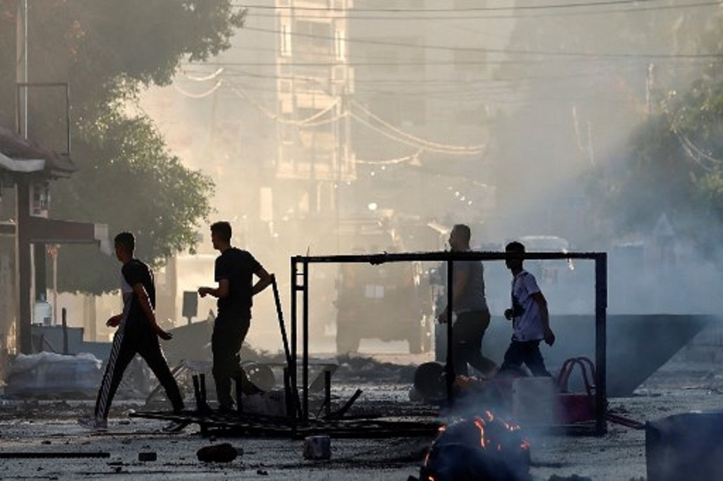 Warga Palestina berjalan melewati objek yang hangus terbakar dalam operasi militer Israel di Jenin, Tepi Barat, 3 Juli 2023. (Jaafar ASHTIYEH / AFP)