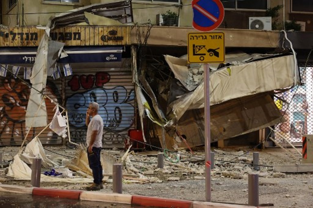 Seorang pria berdiri di depan toko yang rusak terkena roket Hamas di Tel Aviv, Israel, 7 Oktober 2023. (JACK GUEZ / AFP)