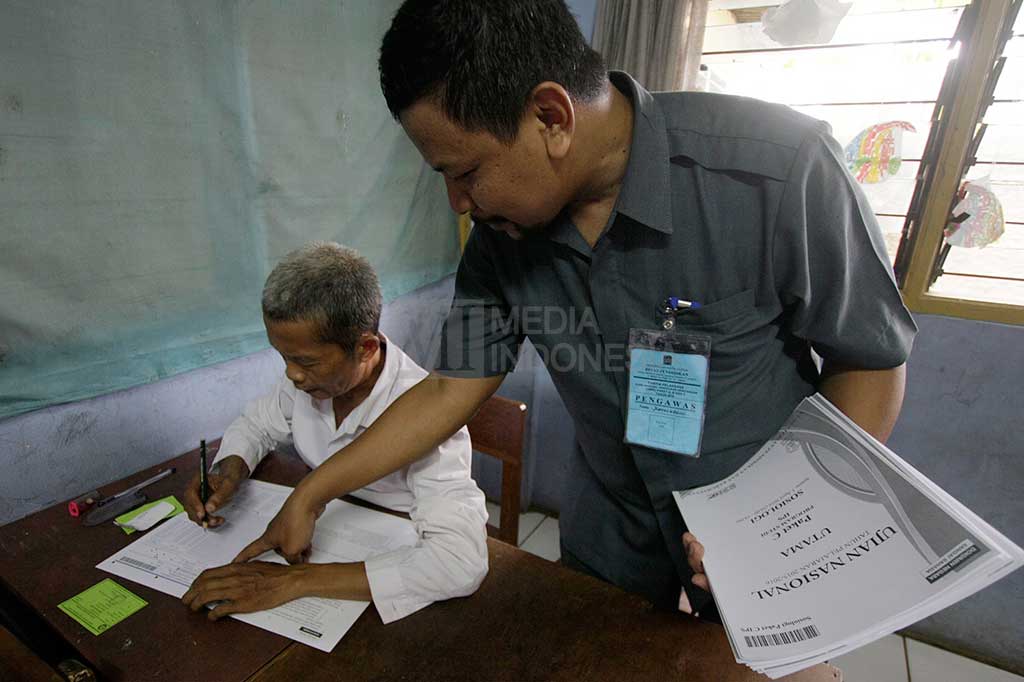 Panita UN membantu menjelaskan cara mengisi lembar jawaban dengan benar kepada Moh. Muhlasin (kiri), salah satu peserta UN tertua di Kota Depok saat mengikuti Ujian Nasional paket C di SMA Al-Muhajirin, Depok, Jawa Barat, Selasa (5/4/2016). 