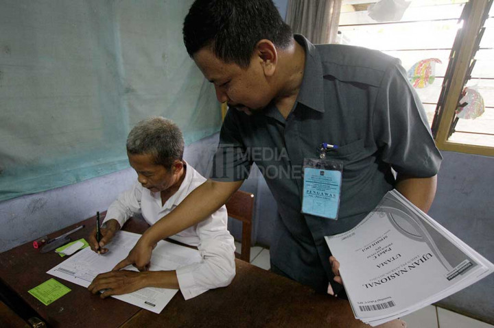 Panita UN membantu menjelaskan cara mengisi lembar jawaban dengan benar kepada Moh. Muhlasin (kiri), salah satu peserta UN tertua di Kota Depok saat mengikuti Ujian Nasional paket C di SMA Al-Muhajirin, Depok, Jawa Barat, Selasa (5/4/2016). 