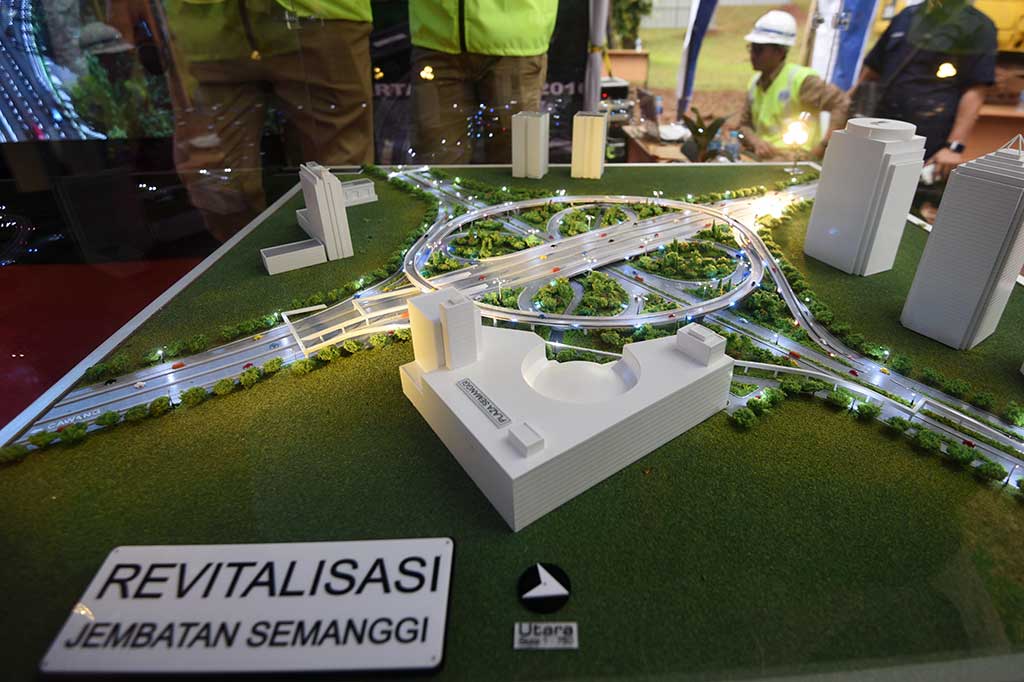 Pekerja berdiri di samping maket proyek jembatan layang simpang susun Semanggi.