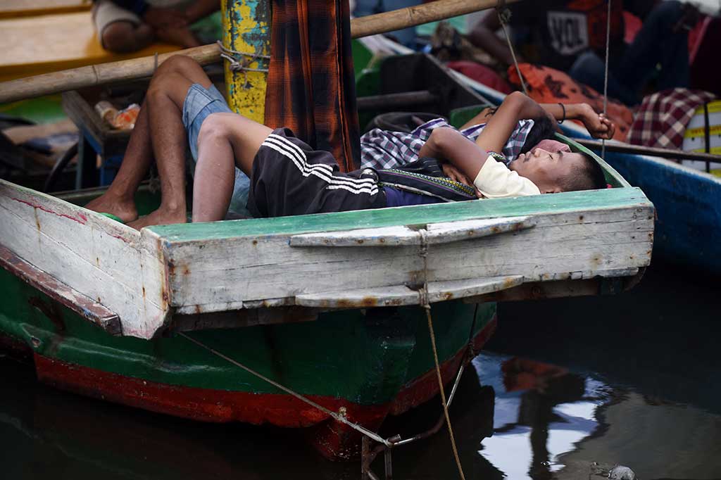 Warga tidur di atas perahu yang bersandar di dermaga.