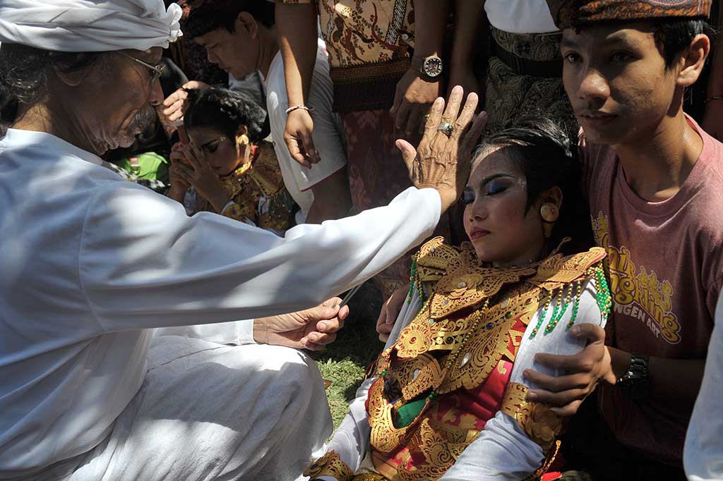 Seorang pemuka agama Hindu menyadarkan penari yang kesurupan.
