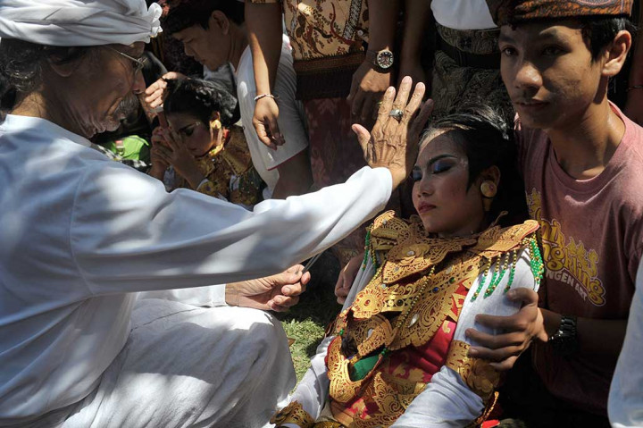 Seorang pemuka agama Hindu menyadarkan penari yang kesurupan.