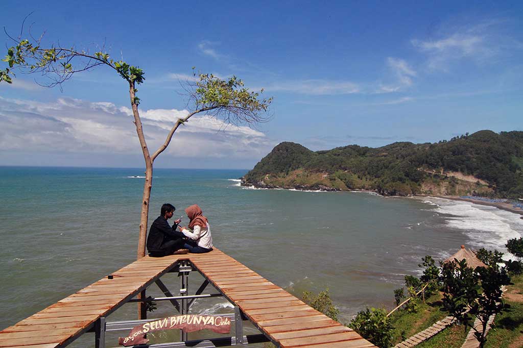 Wisatawan menikmati pemandangan dari atas bukit di kawasan Pantai Watu Bale