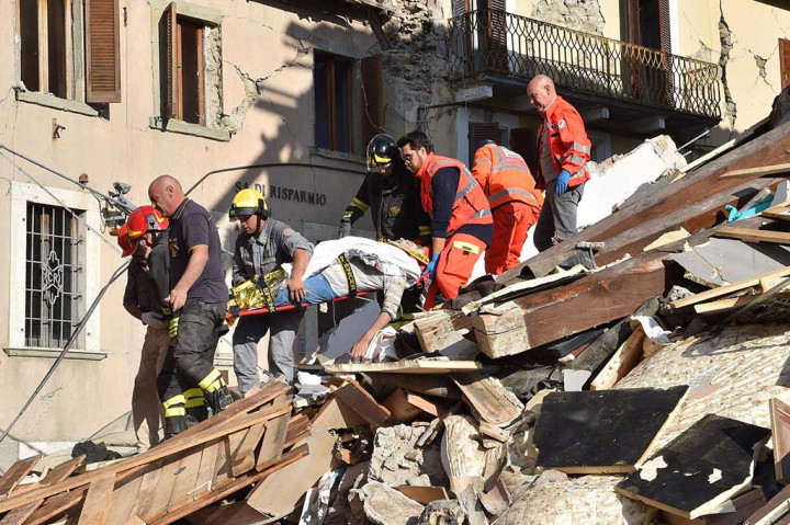 Tim penyelamat mengevakuasi seorang pria di atas tandu di antara bangunan yang rusak di Amatrice.