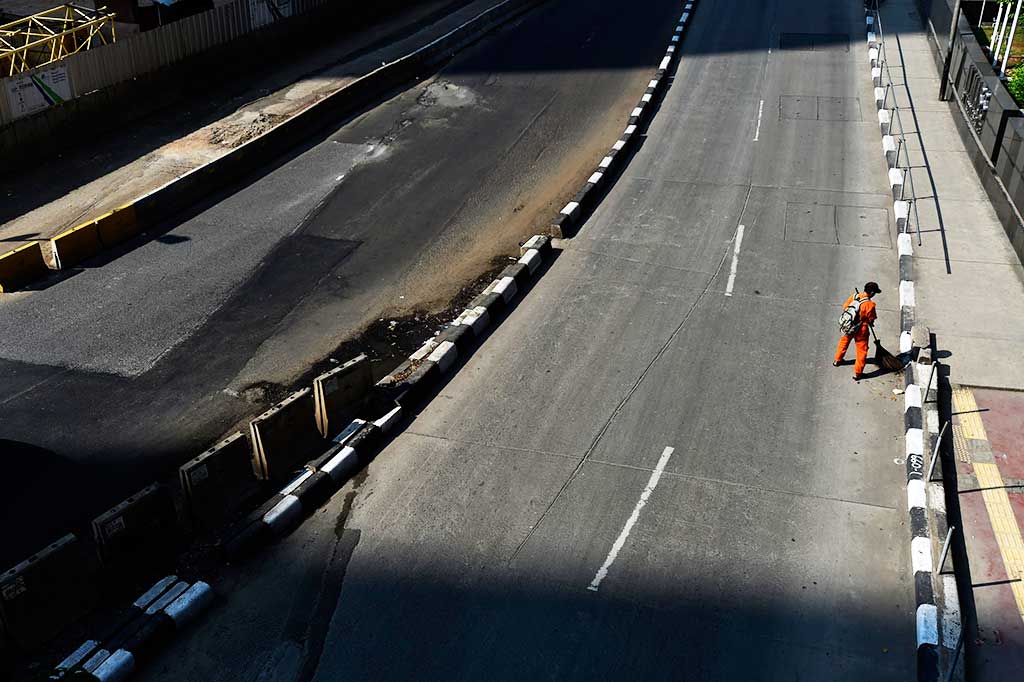 Petugas kebersihan membersihkan Jalan Jenderal Sudirman yang lengang. 