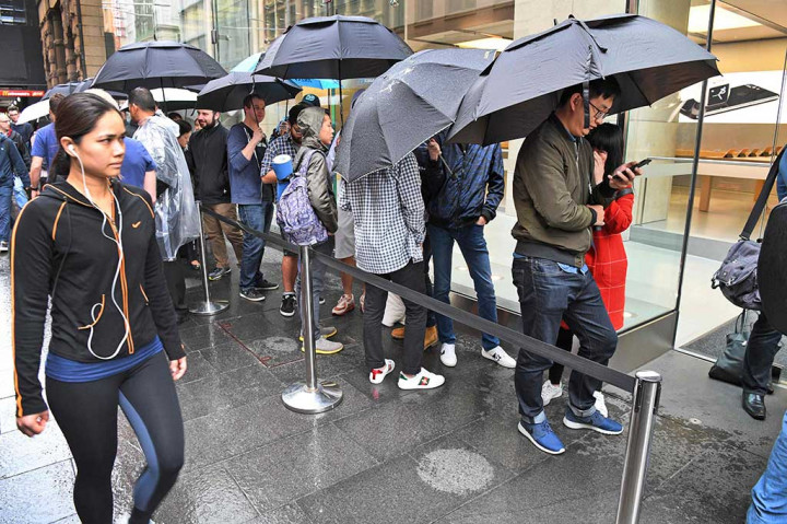 Pembeli antre sambil berpayung di luar toko Apple di kawasan pusat bisnis di Sydney, Australia.