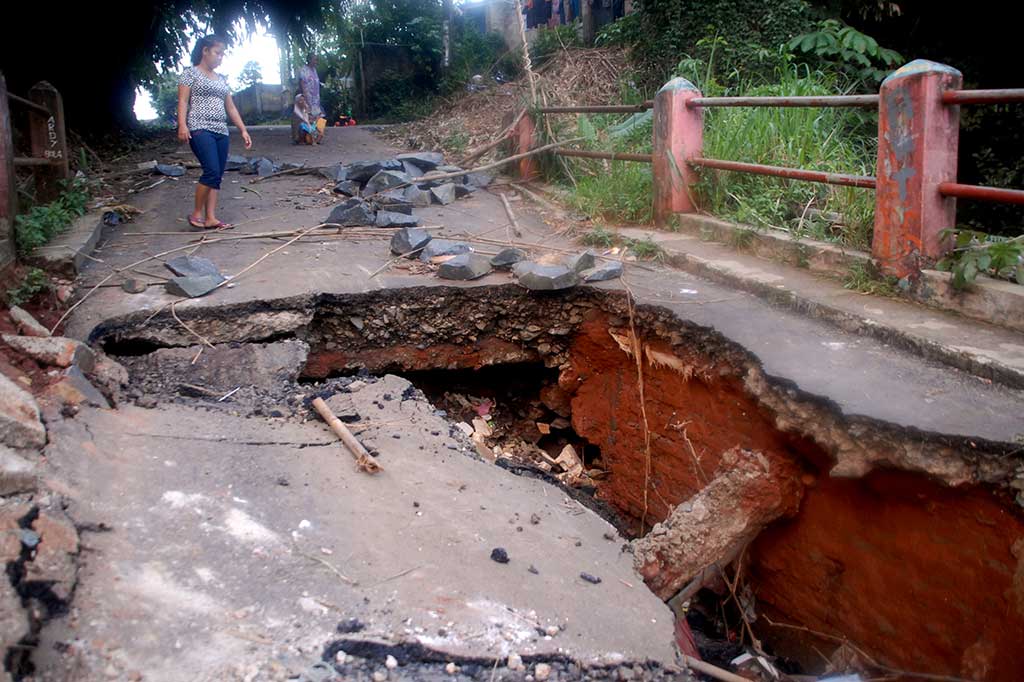Warga melintasi jembatan yang ambles di Jalan Pitara, Pancoran Mas, Depok.