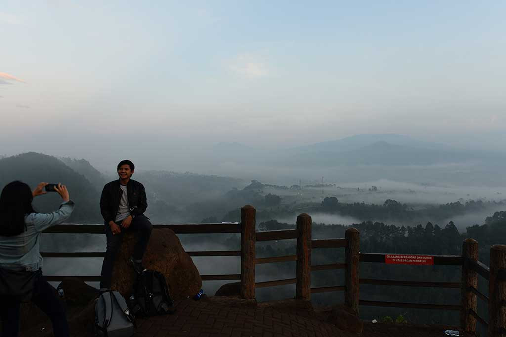 Seorang wisatawan memotret rekannya dengan smartphone dengan latar belakang pemandangan yang indah dan berkabut.