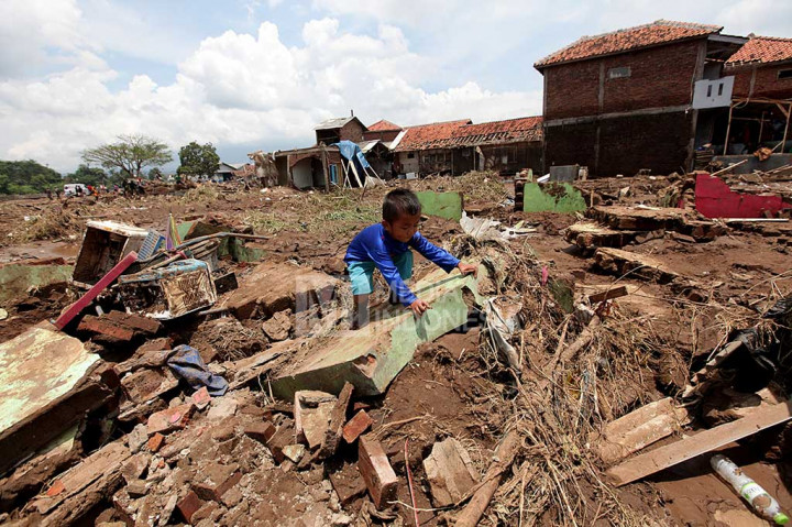 Seorang anak bermain di reruntuhan rumah yang luluh lantak diterjang banjir bandang.