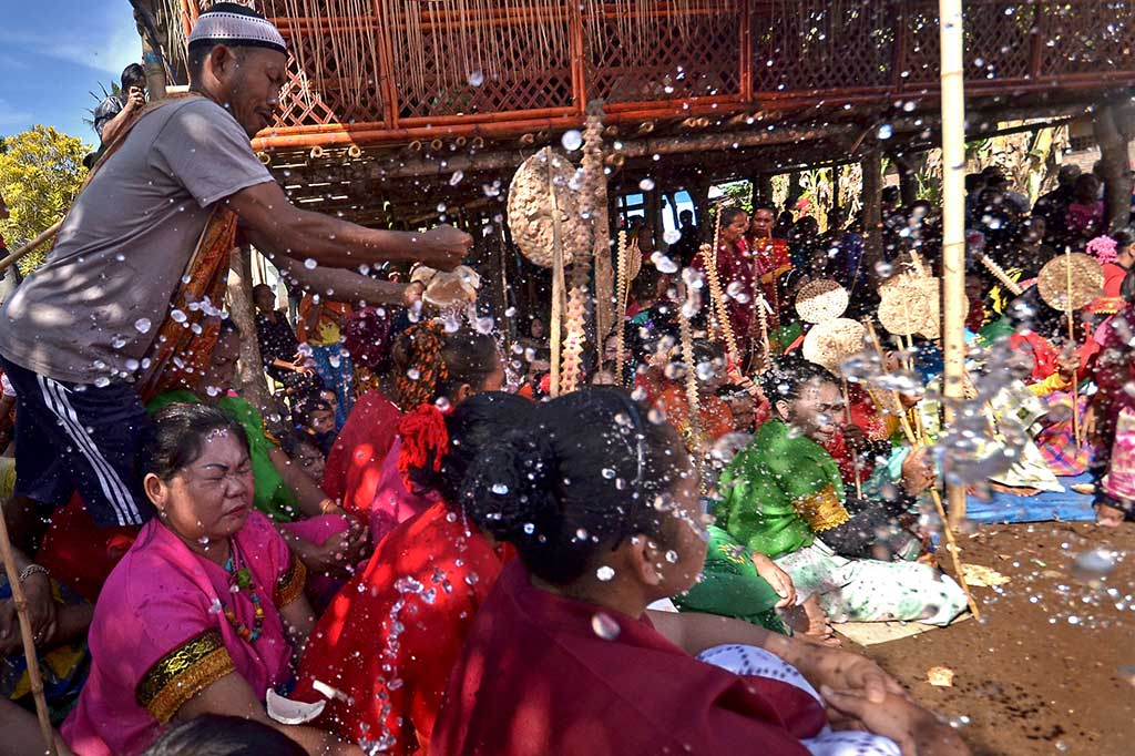 Seorang warga memecahkan kelapa muda dan menyiramkan airnya kepada warga lain pada rangkaian tradisi Pattakkang di Dusun Borong Rappo, Desa Sokkolia, Bontomarannu, Kabupaten Gowa, Sulawesi Selatan, Jumat (23/9/2016).