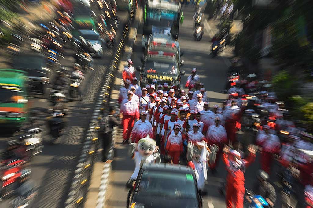 Tim pembawa obor Kirab Peparnas XV berjalan melintasi Jalan Merdeka, Bandung.