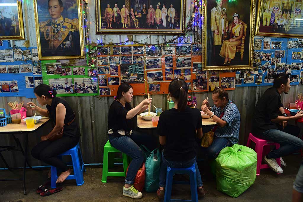Warga Thailand mengenakan pakaian hitam saat makan di sebuah restoran yang memasang foto mendiang Raja Bhumibol Adulyadej.