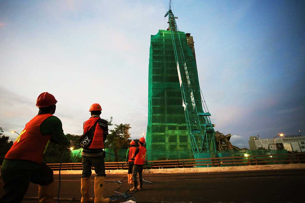 Pekerja menarik kait karung pasir untuk diangkut dengan crane ke atas gedung.