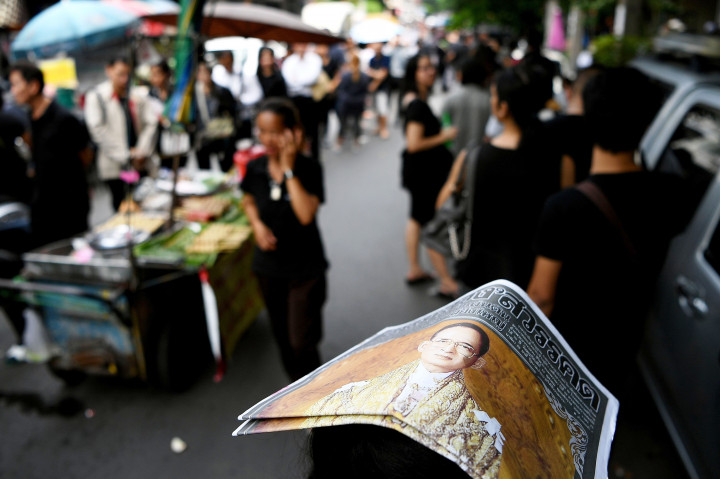 Seorang warga menutupi kepalanya dengan koran yang memasang foto Raja Bhumibol Adulyadej di halaman depan. Selama 70 tahun kepemimpinannya, Raja Bhumibol Adulyadej (88) berhasil menjaga persatuan Thailand dari rentetan konflik pemerintahan dan kudeta militer. AFP PHOTO / MANAN VATSYAYANA