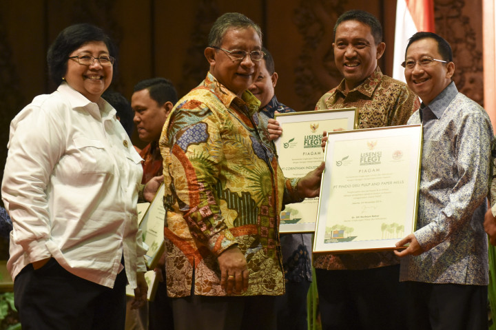Menko Perekonomian Darmin Nasution (kedua kiri) didampingi Menteri Lingkungan Hidup dan Kehutanan Siti Nurbaya (kiri) memberikan penghargaan kepada Direktur PT Pindo Deli Pulp and Paper Suhendra Wiriadinata (kanan) dan perwakilan sembilan perusahaan eksportir produk kayu ke Uni Eropa lainnya saat Perayaan Lisensi FLEGT di Kementerian LHK, Jakarta.