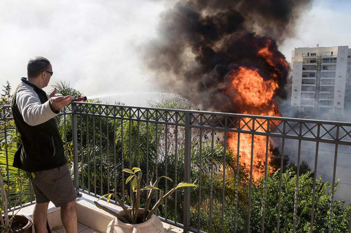 Warga berusaha memadamkan api dengan peralatan sederhana dari atas rumahnya di Kota Haifa.