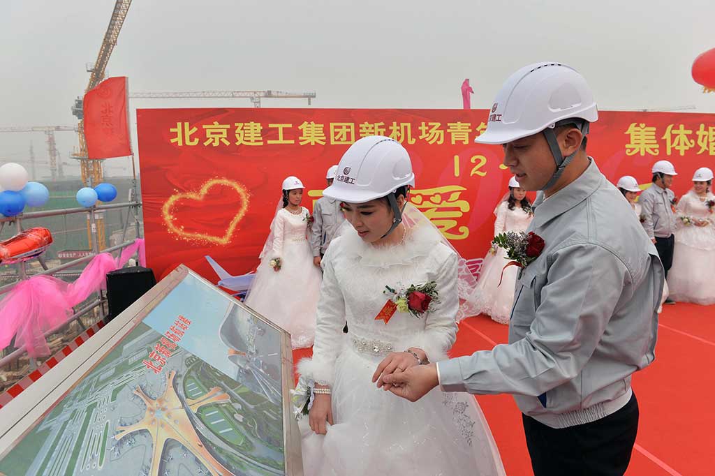 Seorang pekerja menunjukkan kepada istrinya maket bandara baru Beijing, selama upacara pernikahan bersama.