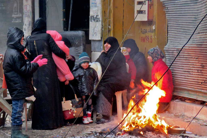 Warga Suriah yang melarikan diri dari daerah bergolak Bustan al-Qasr menghangatkan badan mereka dengan membakar sampah di kawasan Fardos, Aleppo.